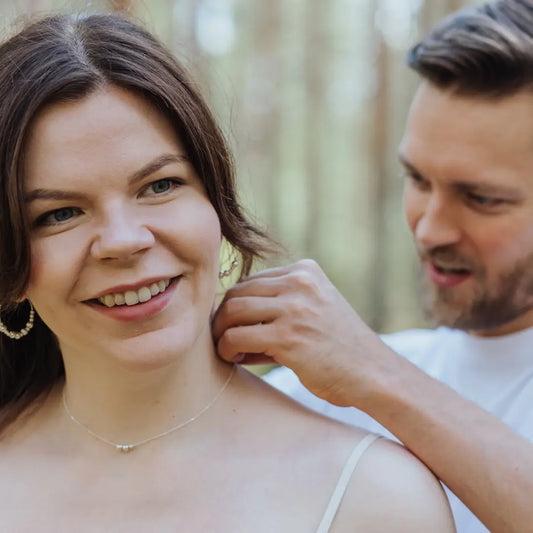 Mies kiinnittää Viesti-kaulakorua naisen kaulaan. Korussa lukee merkityksellinen sana morseaakkosilla kirjoitettuna.